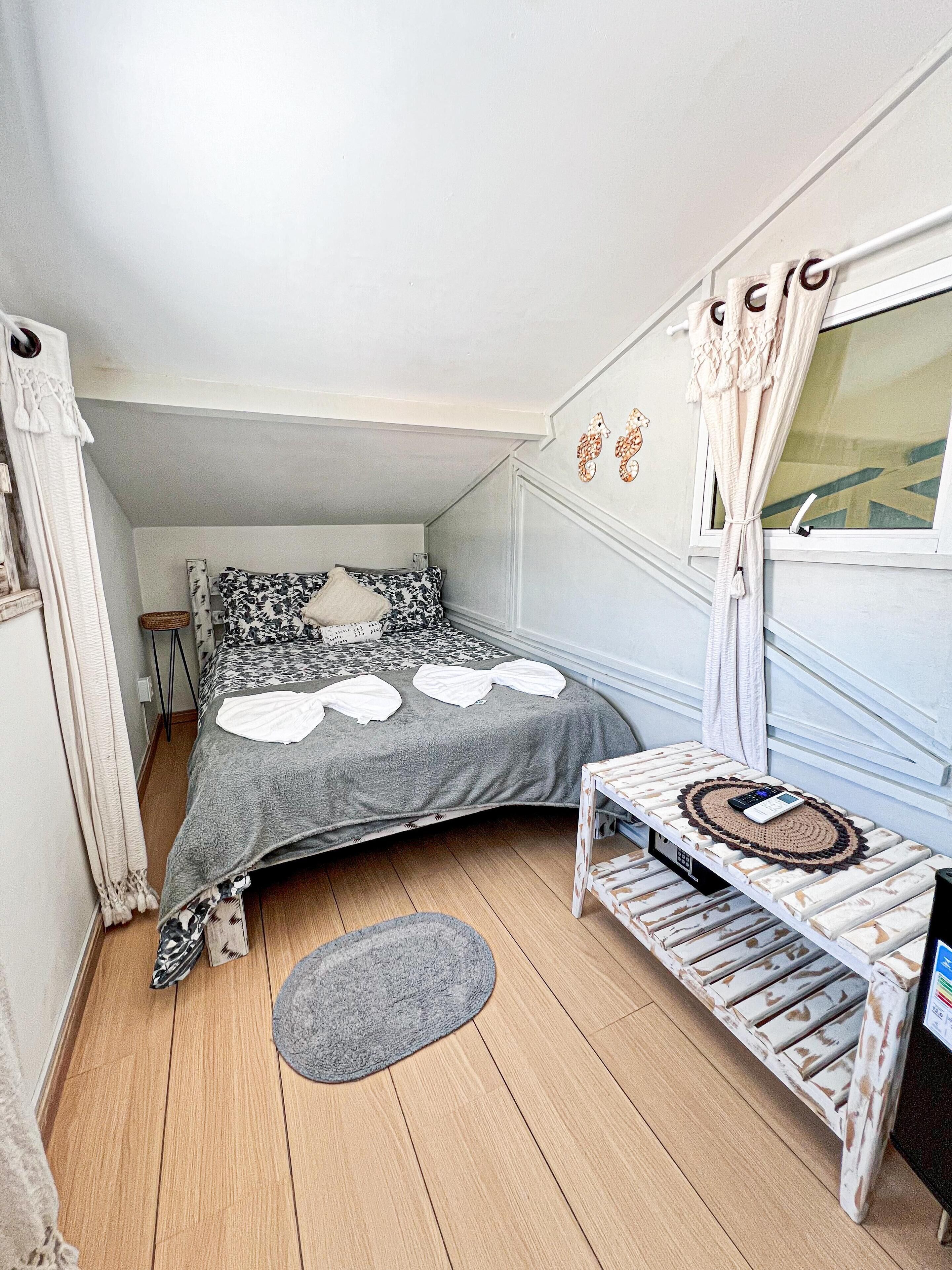 A bedroom with a bed, a small table, a rug, and a window with curtains.