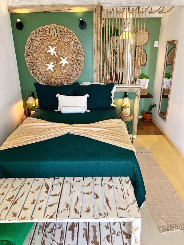 A bed with a dark green bedspread, white pillows, and a woven headboard.