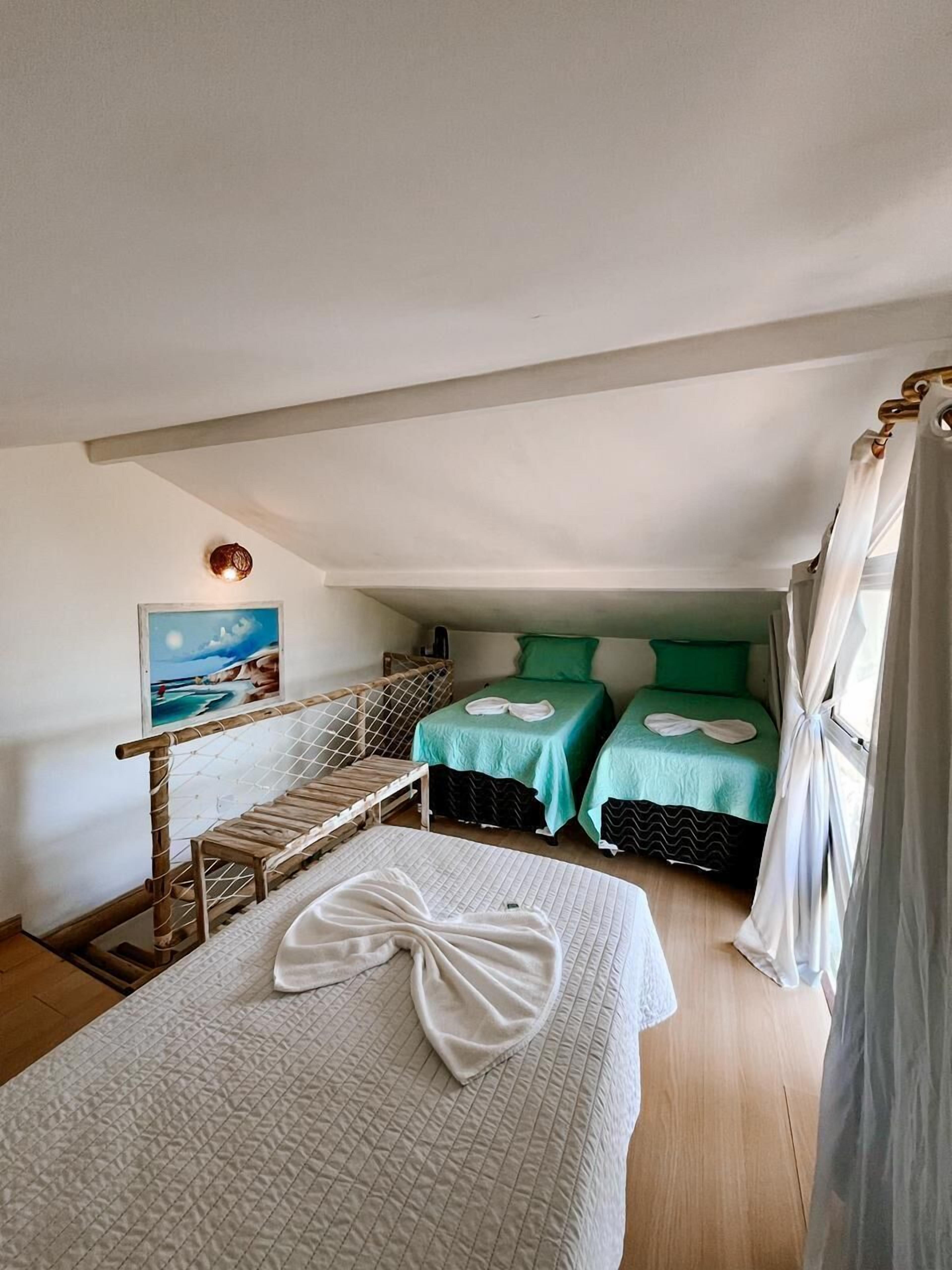 Una habitación con dos camas, una escalera de madera, un cuadro y una ventana con cortinas.