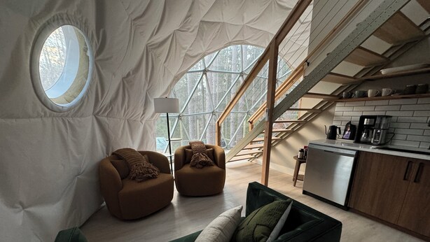 A cozy living area with a green sofa, two brown armchairs, a white lamp, and a kitchen area with a coffee maker and cabinets. - Löyly Luxury Dome, Hot Tub, Sauna, Plunge, King, Queen, Kitchen, Sleeps 4, N. MI (Benzonia)