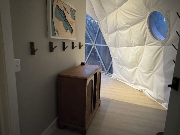 Una estructura tipo tienda con un ventanal circular, un armario de madera y una obra de arte en la pared.