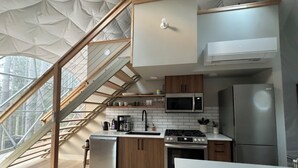 A modern kitchen with a wooden staircase, stainless steel appliances, and a view of the outdoors. - Löyly Luxury Dome, Hot Tub, Sauna, Plunge, King, Queen, Kitchen, Sleeps 4, N. MI (Benzonia)