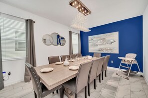 A dining room with a large wooden table set for six, surrounded by six chairs, a baby high chair, and a chandelier. - Marvel Game Room • Poolside Theater • Private Pool & Spa • Near Disney • Resort (Davenport)