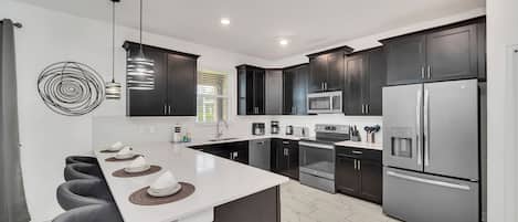 Una cocina moderna con armarios oscuros, electrodomésticos de acero inoxidable y una isla central con taburetes de bar.