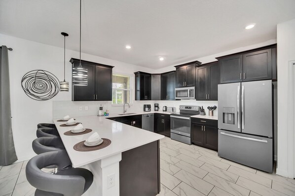 A modern kitchen with dark cabinets, stainless steel appliances, and a central island with bar stools. - Marvel Game Room • Poolside Theater • Private Pool & Spa • Near Disney • Resort (Davenport)