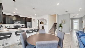 Une cuisine moderne avec des meubles de couleur sombre, un îlot central et un coin repas comprenant une table ronde et des chaises.