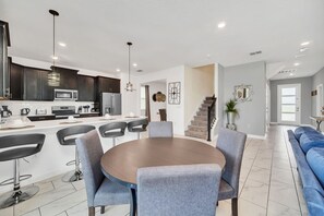 A modern kitchen with dark cabinets, a central island, and a dining area with a round table and chairs. - Marvel Game Room • Poolside Theater • Private Pool & Spa • Near Disney • Resort (Davenport)