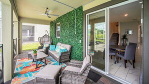 Une terrasse extérieure avec des meubles en osier, un ventilateur de plafond et un mur végétal.