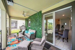 An outdoor patio with wicker furniture, a ceiling fan, and a green wall. - Marvel Game Room • Poolside Theater • Private Pool & Spa • Near Disney • Resort (Davenport)