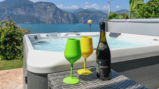 A hot tub with two colorful glasses and a bottle of wine, set against a scenic mountain backdrop. - VILLA MIMOSA - Stunning lake view, private garden, swimming pool and Jacuzzi (Brenzone sul Garda)