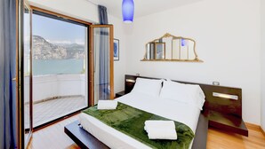 A bedroom with a bed, a nightstand, a mirror, and a view of the sea through a sliding door. - VILLA MIMOSA - Stunning lake view, private garden, swimming pool and Jacuzzi (Brenzone sul Garda)
