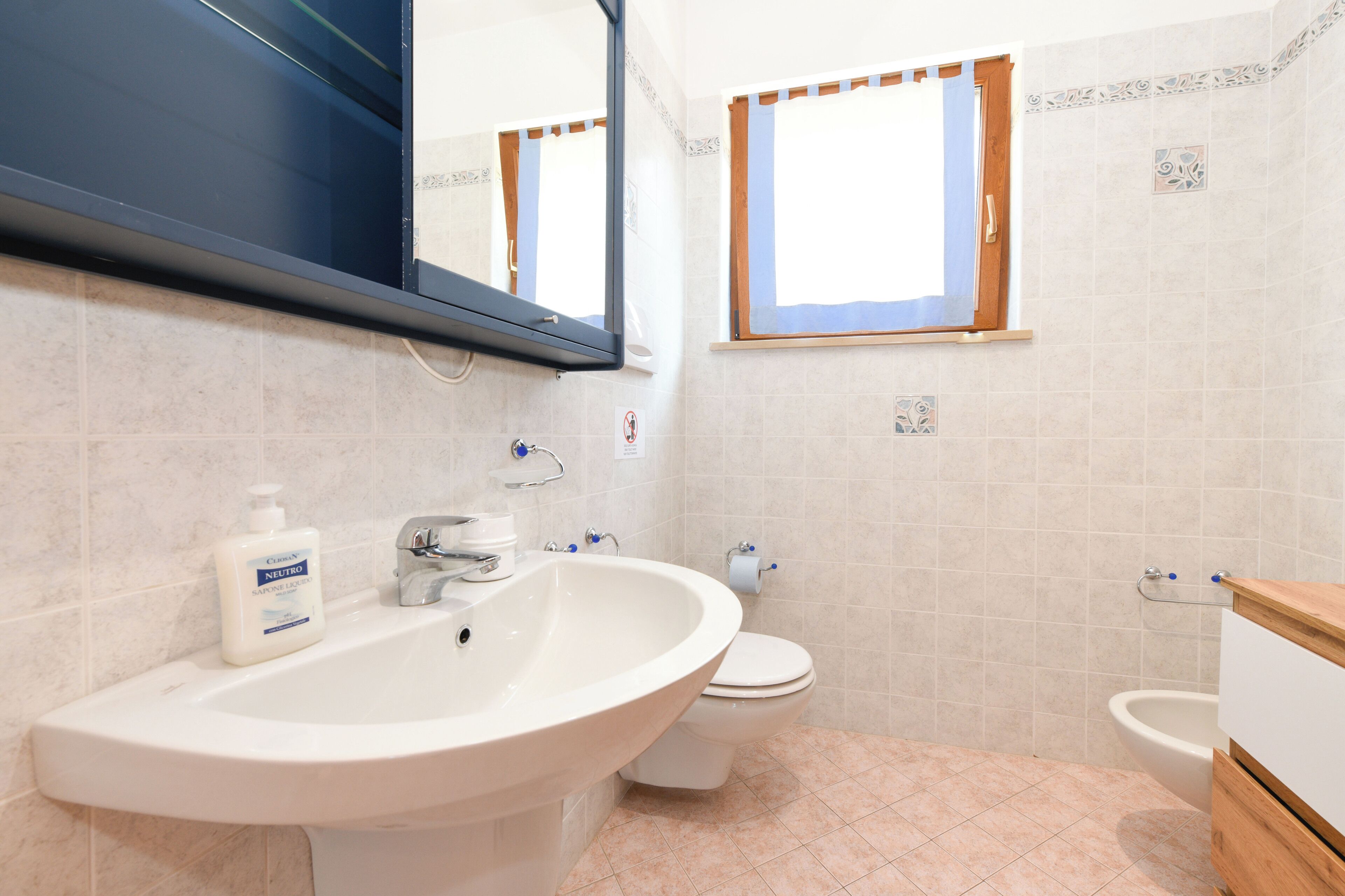 Een badkamer met een groot wastafel, toilet, bidet en een spiegel boven de wastafel.