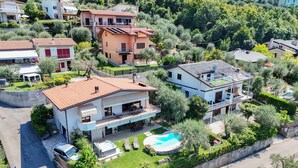A residential area with houses surrounded by greenery, a swimming pool, and a road. - VILLA MIMOSA - Stunning lake view, private garden, swimming pool and Jacuzzi (Brenzone sul Garda)