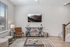 A living room with a wooden coffee table, a sofa, a TV mounted on the wall, and a bookshelf.