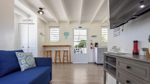 Ein Zimmer mit einem blauen Sofa, einer Küchenzeile mit Hockern, einem Wäschezeichen und einer Stranddekoration.