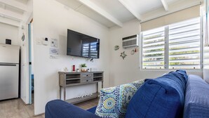 Ein modernes Wohnzimmer mit einer Couch, einem Flachbildfernseher, einem kleinen Tisch und einem Fenster mit Jalousien.