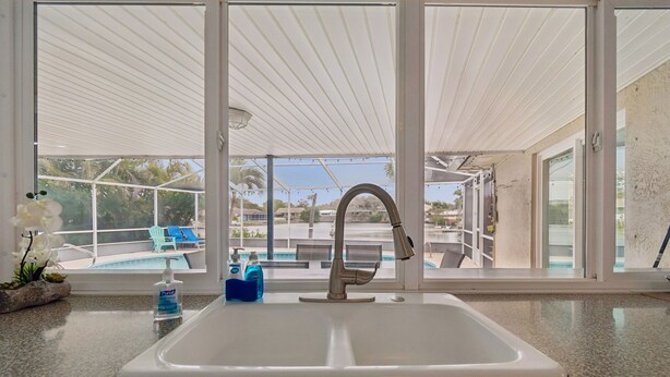 A kitchen with a white sink, granite countertop, and a view of a pool and palm trees. - Waterfront Pool Home - 12PPL 4BR (Clearwater)