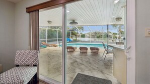 A room with a sliding glass door leading to a pool area with lounge chairs and a ceiling fan. - Waterfront Pool Home - 12PPL 4BR (Clearwater)