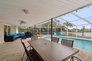 A covered outdoor area with a pool, a table, and a sofa.