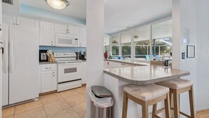 A modern kitchen with white cabinets, a stainless steel trash bin, a granite countertop, and a view of the outdoors. - Waterfront Pool Home - 12PPL 4BR (Clearwater)
