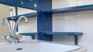 Un lavabo de salle de bain avec un robinet chromé, des poutres de soutien bleues et un mur recouvert de carreaux blancs.