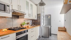 Una cocina moderna con armarios blancos, encimera de madera, horno empotrado, refrigerador de acero inoxidable y una lámpara colgante.