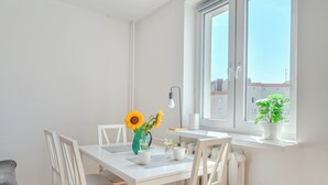 Un comedor luminoso con una mesa blanca, sillas y un jarrón con girasoles.