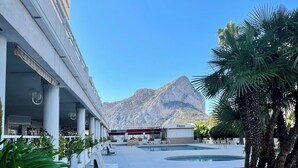 A hotel courtyard with a pool, palm trees, and a mountain backdrop. - First-line sea views -  One bedroom modern cosy apartment (Calp)