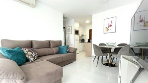 A modern living room with a beige sectional sofa, a dining table with chairs, and a kitchen area in the background. - First-line sea views -  One bedroom modern cosy apartment (Calp)
