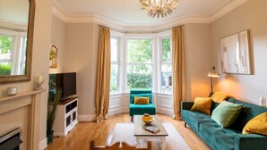 A living room with a fireplace, a green sofa, a dining table, and a chandelier. - Cosy Flat in the Heart of Jesmond - Pass the Keys (Newcastle)