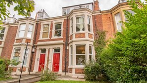 A row of terraced houses with bay windows, red doors, and a well-maintained lawn. - Cosy Flat in the Heart of Jesmond - Pass the Keys (Newcastle)
