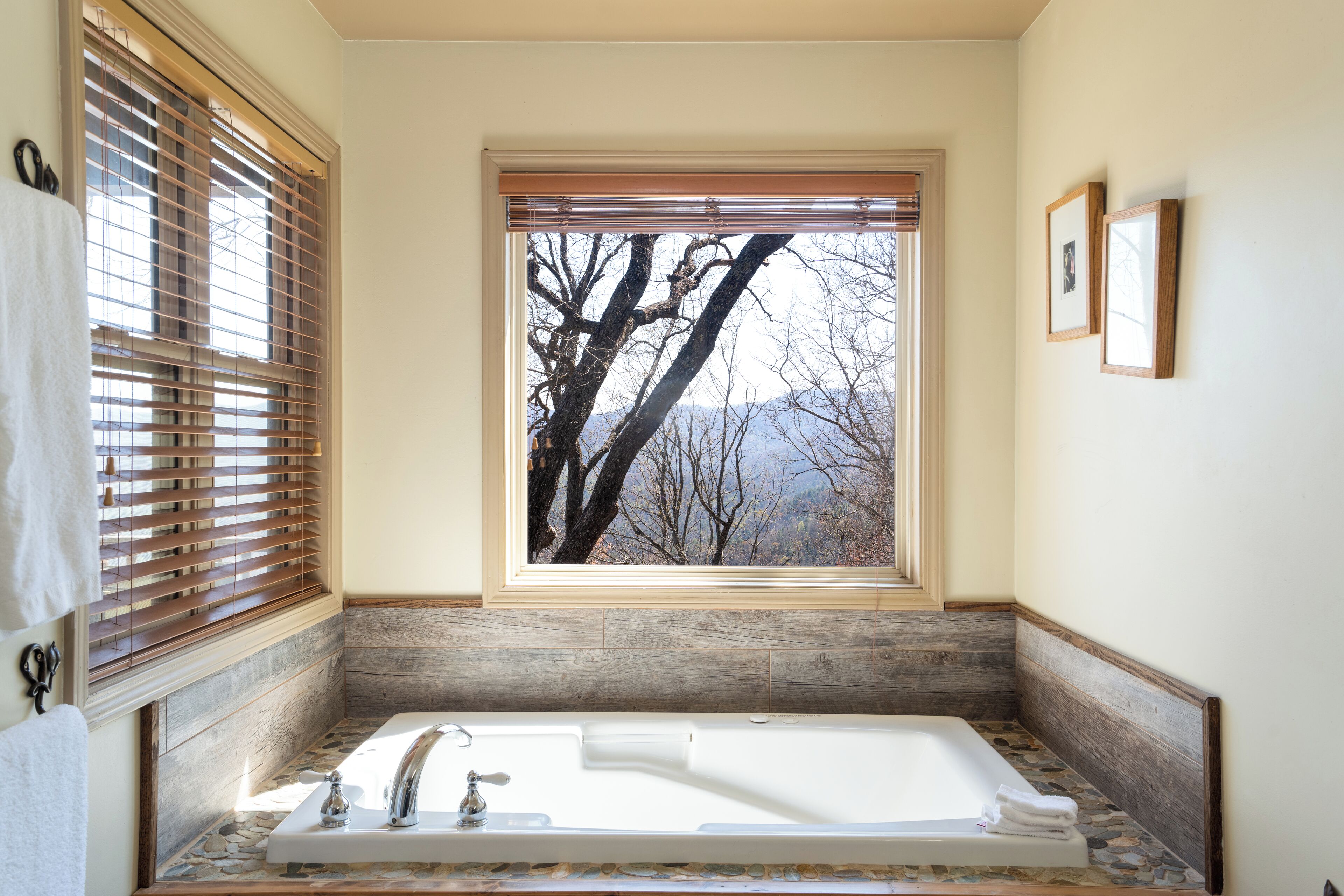 Un baño con una bañera grande, detalles de madera, un ventanal con vistas a árboles y montañas, y un perchero para toallas.