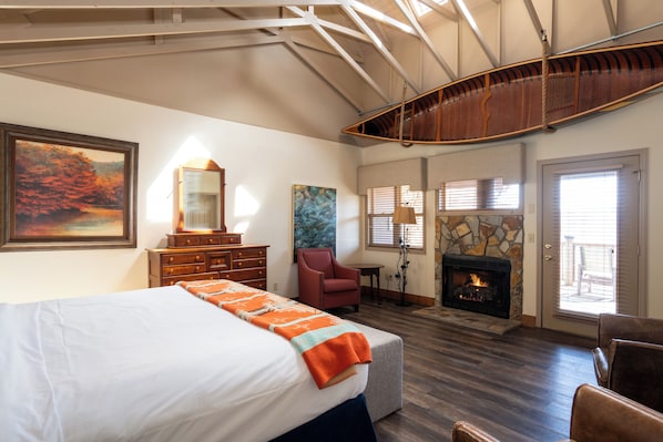 A bedroom with a bed, a fireplace, a stone wall, and a large window. - Snowbird Mountain Lodge (Robbinsville)