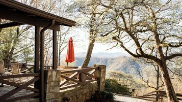 A wooden deck with chairs and an umbrella, overlooking a mountainous landscape.