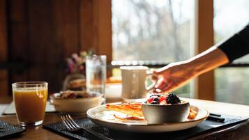 A breakfast setting with a plate of pancakes, a bowl of fruit, and a glass of orange juice on a wooden table.