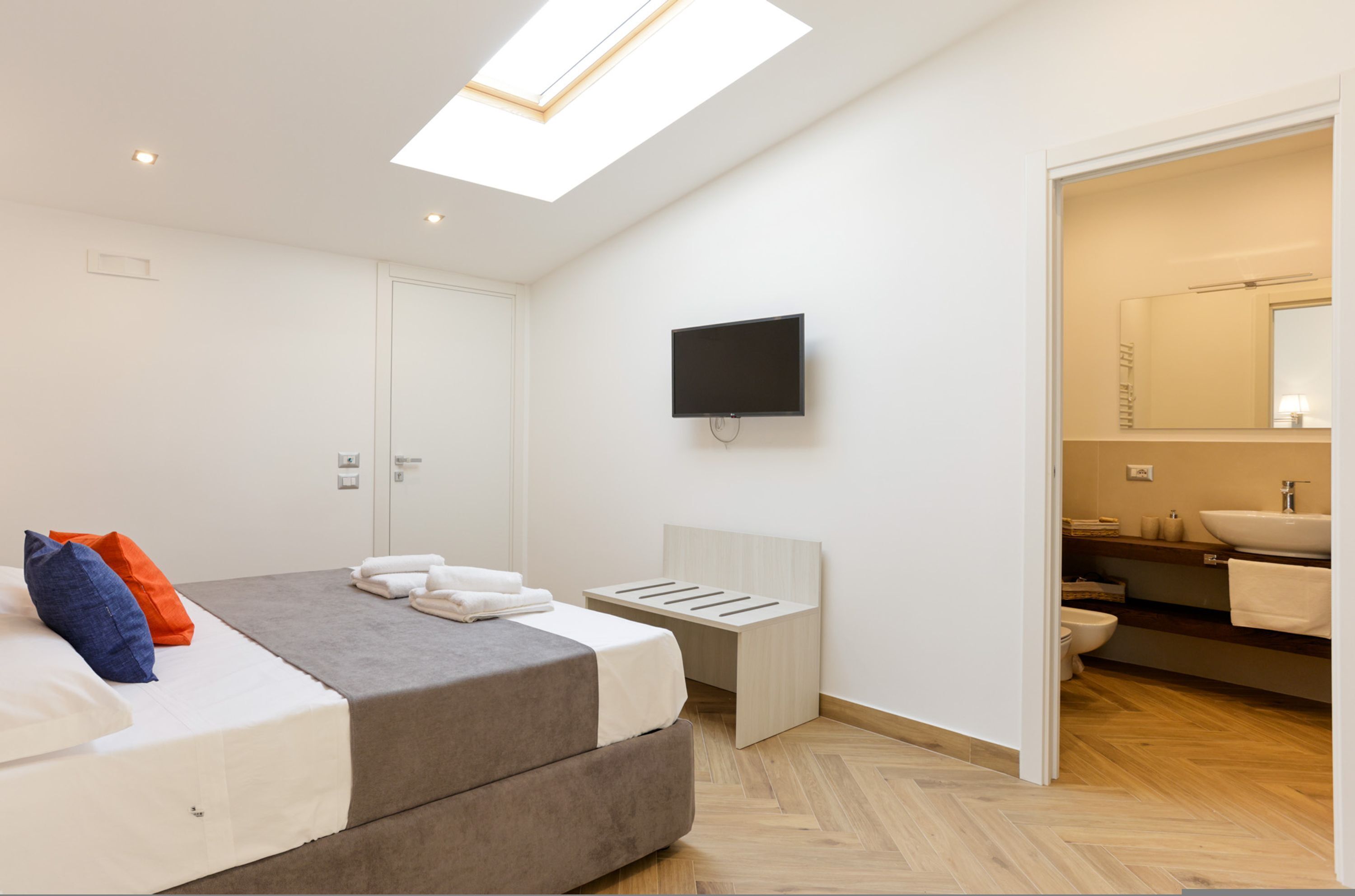 Ein modernes Schlafzimmer mit einem Bett, einem Fernseher und einem durch eine offene Tür einsehbaren Badezimmer.