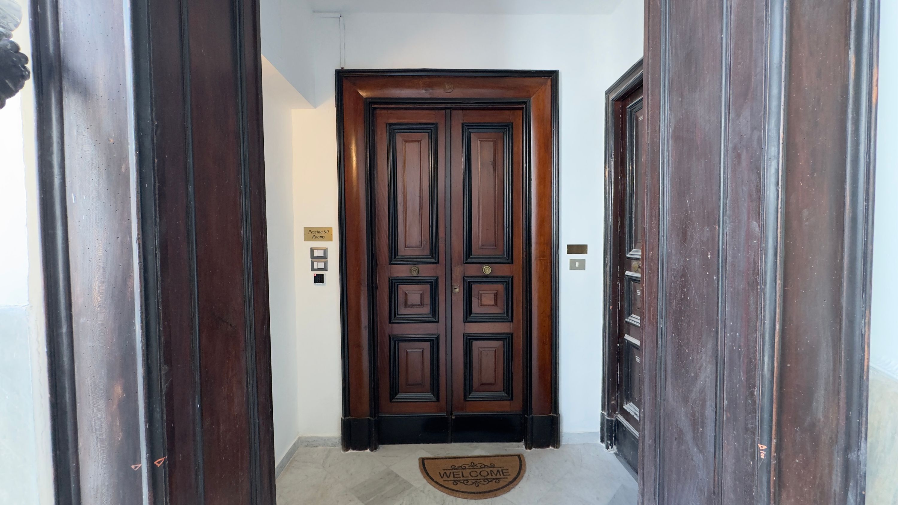 Uma porta dupla de madeira com uma placa indicando 'Pessina 90 Rooms'.