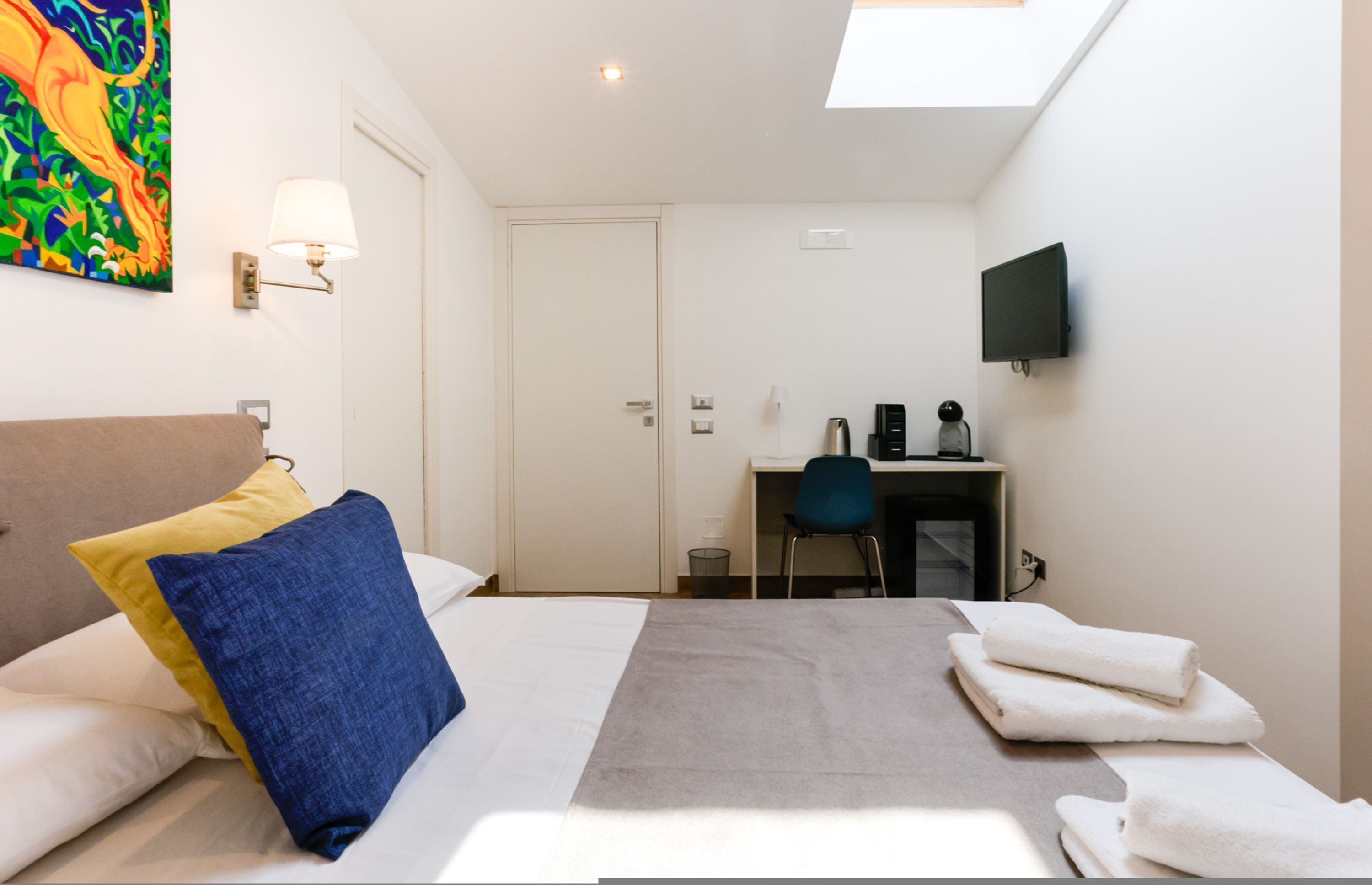 A hotel room with a bed, a desk, a chair, a TV, and a painting on the wall.