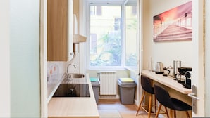 Een kleine keuken met een raam, een radiator en een eethoek met stoelen.