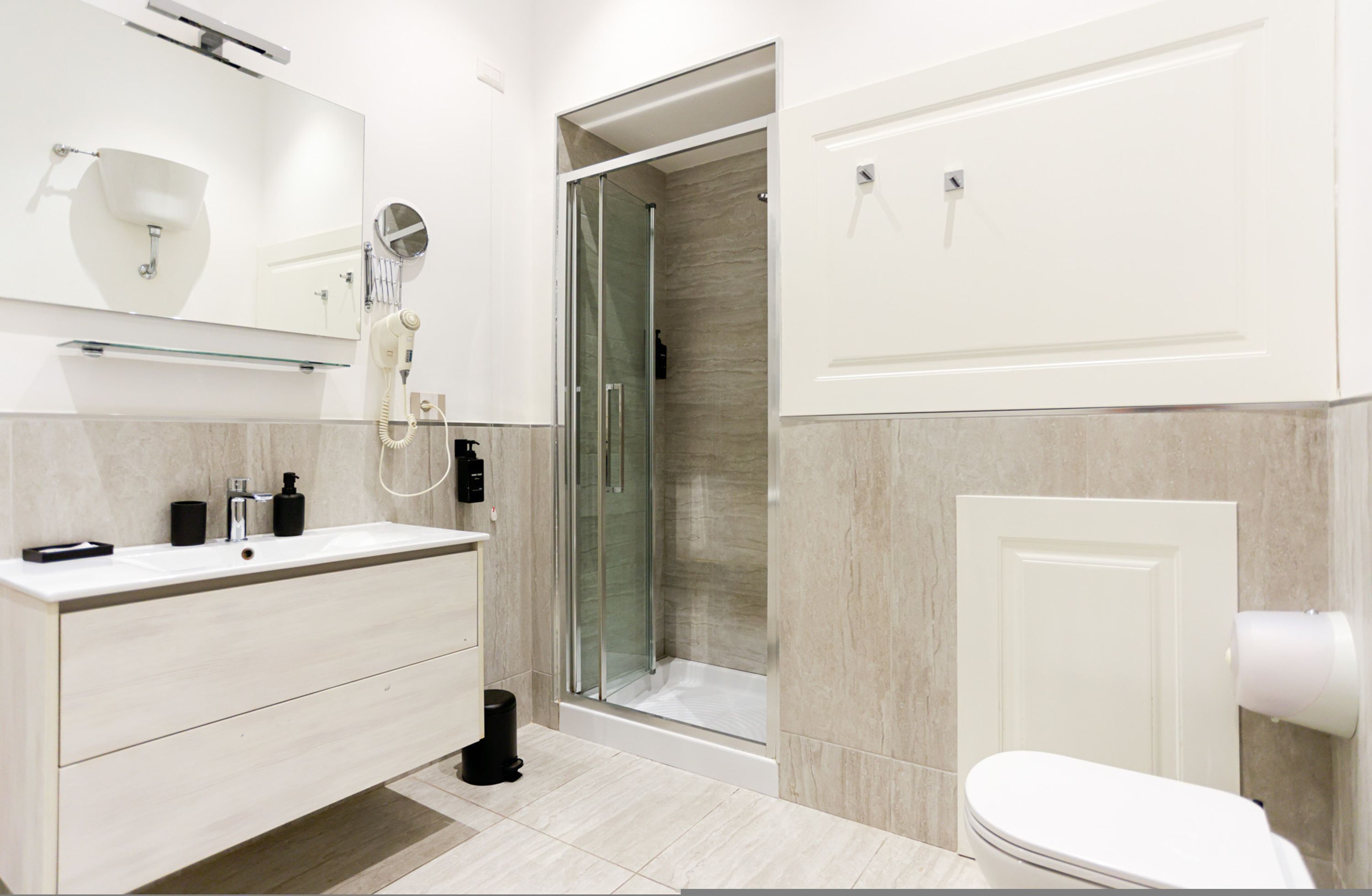 A modern bathroom with a glass-enclosed shower, a white sink with a mirror above it, and a toilet with a paper towel dispenser.