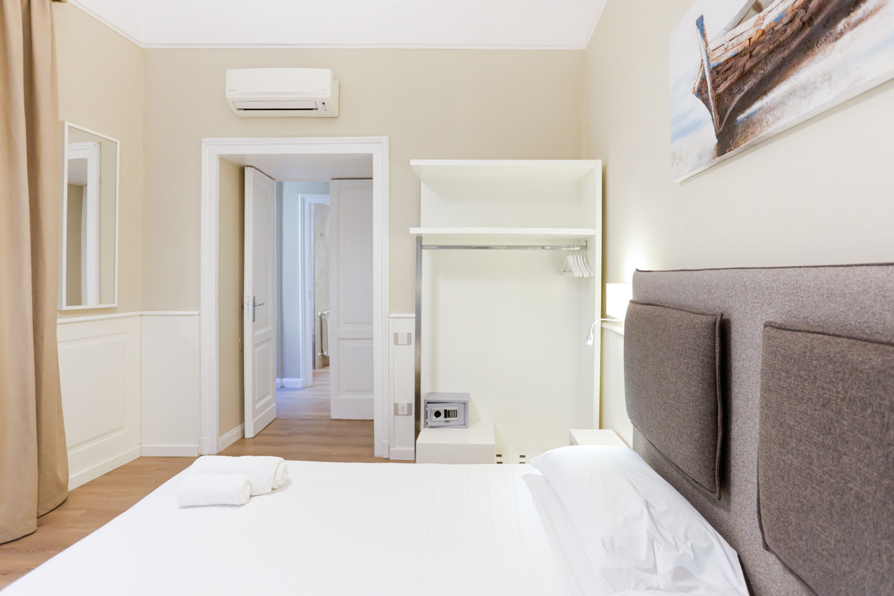 A hotel room with a bed, a wardrobe, an air conditioning unit, and a painting on the wall.
