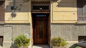 Une entrée d’immeuble avec une porte en bois, une petite fenêtre au-dessus de la porte et le chiffre « 16 » peint sur le mur.
