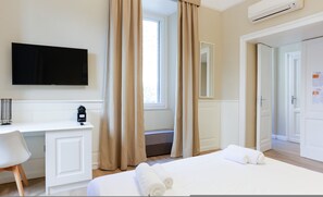A hotel room with a bed, a desk, a TV, a window with curtains, and an air conditioning unit. - Il Centrale - Camera 3 (Naples)