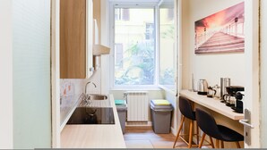 Une cuisine compacte avec une fenêtre, un radiateur et un petit coin bar équipé de tabourets.
