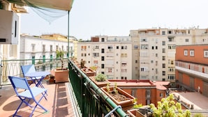 A balcony with blue chairs and potted plants, overlooking a row of buildings. - Riviera di Chiaia 207 (Naples)