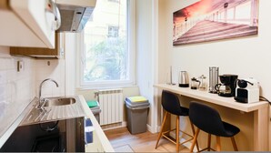 A compact kitchen with a window, a sink, a radiator, a trash bin, and a bar area with chairs and a coffee machine. - Il Centrale in Naples (Naples)