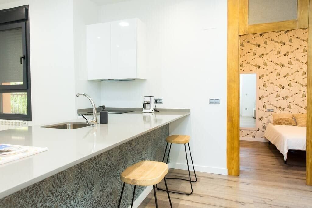 Une cuisine moderne avec un plan de travail blanc, un évier en acier inoxydable et deux tabourets en bois.