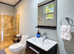 A modern bathroom with a shower, toilet, sink, and a window providing natural light.