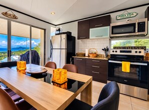 A modern kitchen with a view, featuring a wooden dining table, dark cabinets, a microwave, and an oven.