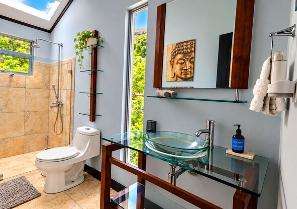 A modern bathroom with a glass sink, a toilet, a shower, and a skylight.